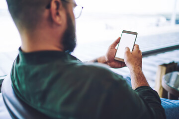 Unshaven man in armchair browsing smartphone