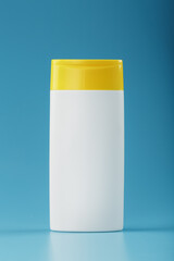 White plastic bottle with yellow cap with shampoo gel on blue background.