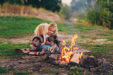 Two children sit near campfire on sunset