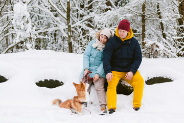 Fototapeta na wymiar Well dressed happy girl and man with Corgi dog outdoors in winter. Pets, people and season concept. Cheerful couple having fun in park