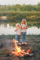 Two little girls is eating marshmallows. The children bakes sweetness at the stake. Vertical view