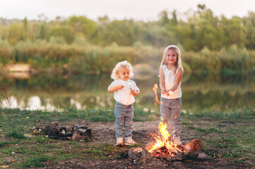 Two little girls is eating marshmallows. The children bakes sweetness at the stake.