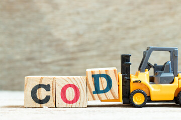 Toy forklift hold letter block D to complete word COD (abbreviation of cash on delivery) on wood...