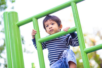 Asian preschool boy climbing on playground climb bar in city public park morning activity