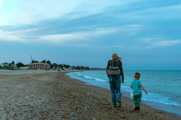 Mom and son in clothes are walking along the sea coast. The interaction of mother and child.