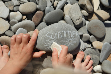 the word summer on a stone on a sunny day on a pebbly sea beach written in chalk