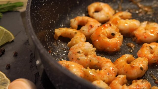 Camera movement of cooking shrimp in sweet and sour sauce with garlic spices and seasonings. Prawns in frying pan on stove on background of lemon, olive oil and rosemary. Food background