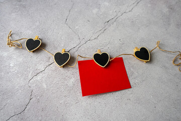 On Valentine's Day, a red sheet of paper hangs on a string of pins with black hearts on a gray...