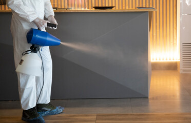 Man in white protective suit in the hotel or hospital sprays hotel rooms, elevator to prevent the...