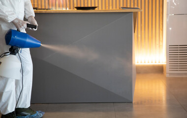 Man in white protective suit in the hotel or hospital sprays hotel rooms, elevator to prevent the...