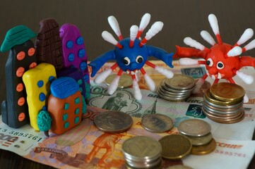 Toy house made of plasticine on the table. Next to the figures of the virus and paper money.