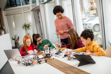 Happy kids with their African American female science teacher with laptop programming electric toys and robots at robotics classroom