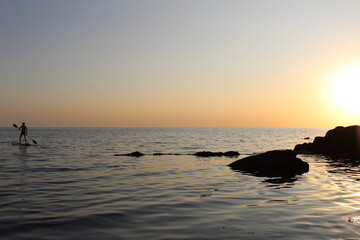Fototapeta na wymiar a man with oars on a board in the sea .beautiful sunset on a mountain beach
