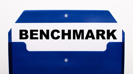 On a white background, a blue folder for papers. In the folder is a sheet of paper with the words BENCHMARK