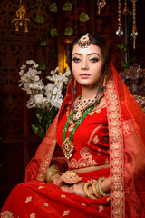 Magnificent young Indian bride in luxurious dress and precious jewellery is sitting in a chair in a luxury apartment. Classic vintage interior. Wedding fashion.