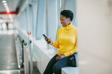 Attractive African girl is waiting for a train in the subway and listening to music with headphones