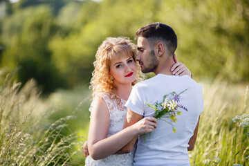 Young man and woman couple walk in the meadow. Tender holding each other. Spring lovestory. Blonde-haired girl with curled hairs and man weared in casual and denim. Young family