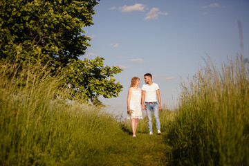 Young man and woman couple walk in the meadow. Tender holding each other. Spring lovestory. Blonde-haired girl with curled hairs and man weared in casual and denim. Young family