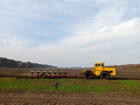 Agricultural yellow tractor, combine rides on the field, handles the ground, plough yells the ground in the fall.