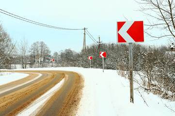 asphalt road in the countryside indicated by a left turn sign sprinkled with sand against the background of a red sign