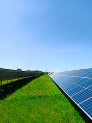 A row of solar panels stand on a green field, against the blue sky. A symbol of clean energy,...