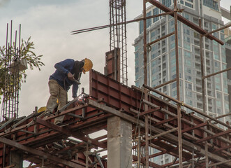 Naklejka premium Construction Worker Welding soldering metal girders and Sparks in a Structure high above at the Construction site. Selective focus.