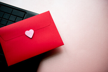 Love letter in a red envelope with a pink heart on a black laptop keyboard, top view