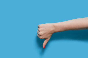 The doing woman shows a dislike sign by putting her thumb down. Female hand with red gel polish manicure on a blue background. Copy space.
