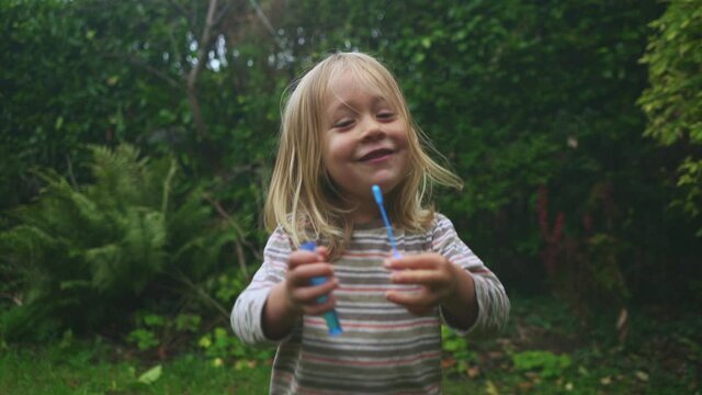 A little preschooler is blowing bubbles in the garden