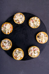 Tartlets with salad on a black board on a concrete background.