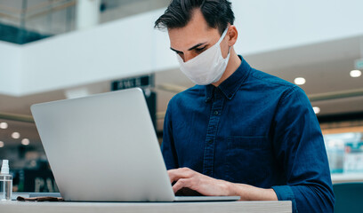 young man in a protective mask sitting in front of an open laptop.