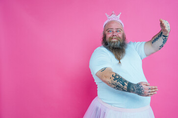 Funny man dancing and having fun wearing  a ballet outfit. Happy princess on a pink colored background