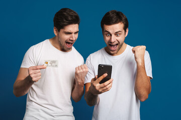 Delighted two guys posing with credit card and mobile phone