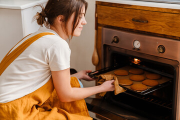 Caucasian pleased pastry chef woman baking cookies at cozy kitchen
