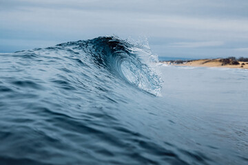 Crashing glassy wave on the sandy beach. Breaking ocean wave, ideal swell for surfing