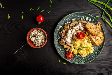 Scrambled Eggs with Mushrooms and Cottage Cheese. Delicious breakfast or snack on a dark background, top view
