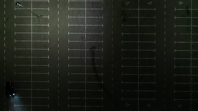 The car on the empty parking at night, aerial shot. Top down, top view, aerial drone footage of a black car driving and parking in a parking lot at night.