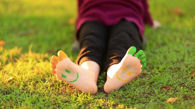 Child having fun with paints in spring park outdoors. Smiley on feet. 