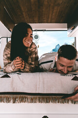 Image of two young Europeans, smiling and looking at the mobile inside a camper van during their trip