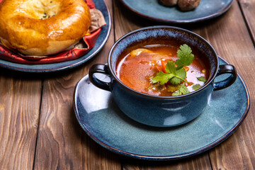 A cup of soup, seasoned with herbs, fresh pastries and fried potatoes with cutlets on a brown wooden background.