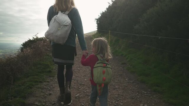 A little preschooler is walking hand in hand with his mother on a hillside in the autumn