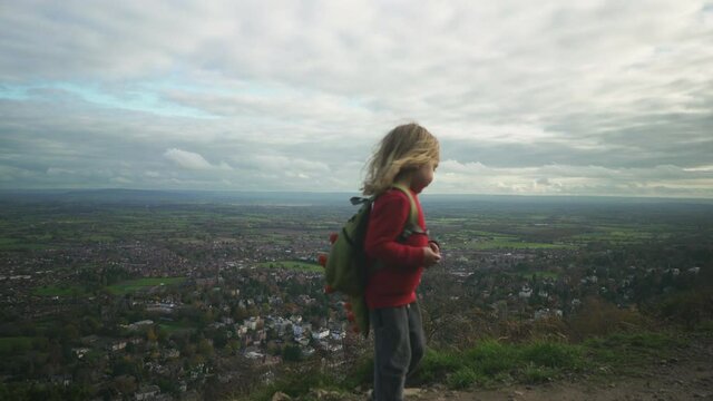A little preschooler is admiring the view from a hilltop before running to his mother