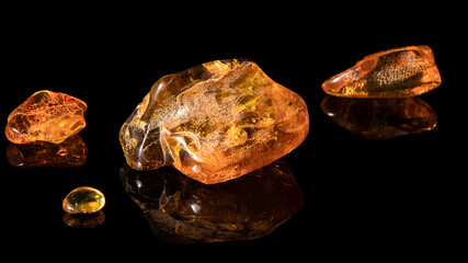 Sparkling big natural  orange and green Baltic amber stone with plant inclusion surrounded by small amber minerals  on a black background with reflection. Material for jewelers, amber texture.