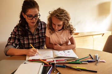 Mother helps her daughter to draw with colored pencils.	
