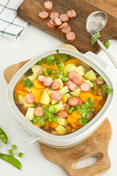 Vegetable soup with sausages in a soup tureen with sausage slices on a wooden board