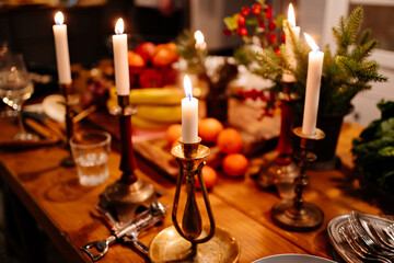Low light. tangerines and apples in a metal basket, burning candles, grapes, bananas, pine branch on the kitchen table. New Year's or Christmas decor. dinner by candlelight in dark. Selective focus.
