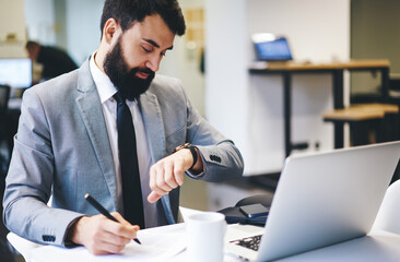 Pensive businessman looking at wristwatch while working in office