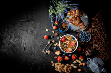 Traditional healthy breakfast foods and drinks - oats, granola, yoghurt, toasts, cereal, croissants, with fruit, berry and coffee on dark background. Diet food or healthy food in the morning