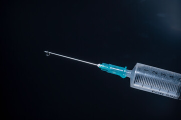 Close-up of a syringe with cannula and drop in front of dark blue background