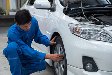 Asian car mechanic technician sitting and checking car tyres or car wheel in in auto repair shop garage. Wheel tire repair service.